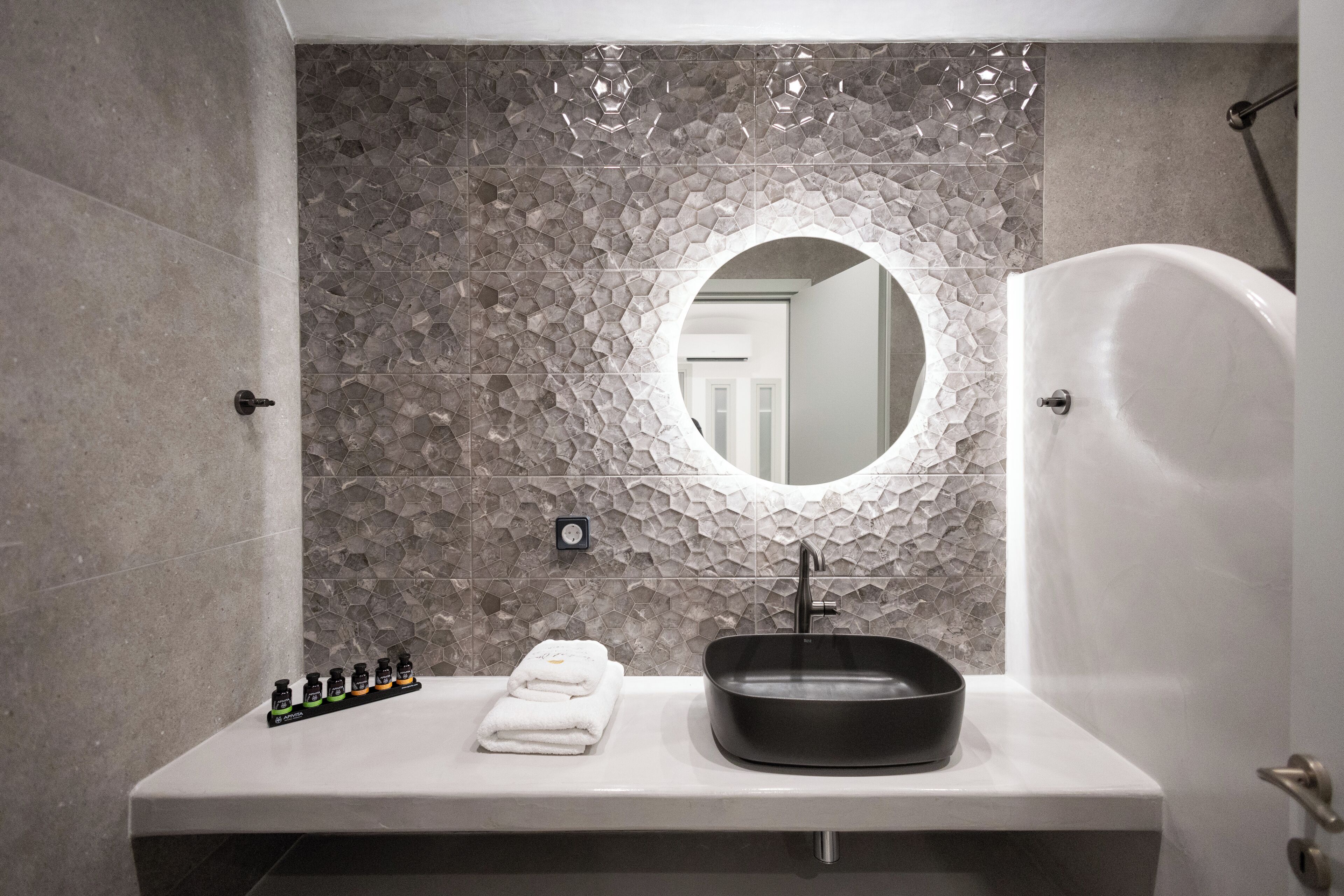 Un baño con un lavamanos moderno, un espejo redondo y una bañera.