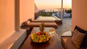 Une terrasse sur le toit avec un plafond en bois, une table sur laquelle se trouve un panier de fruits, deux verres et un canapé avec des coussins.