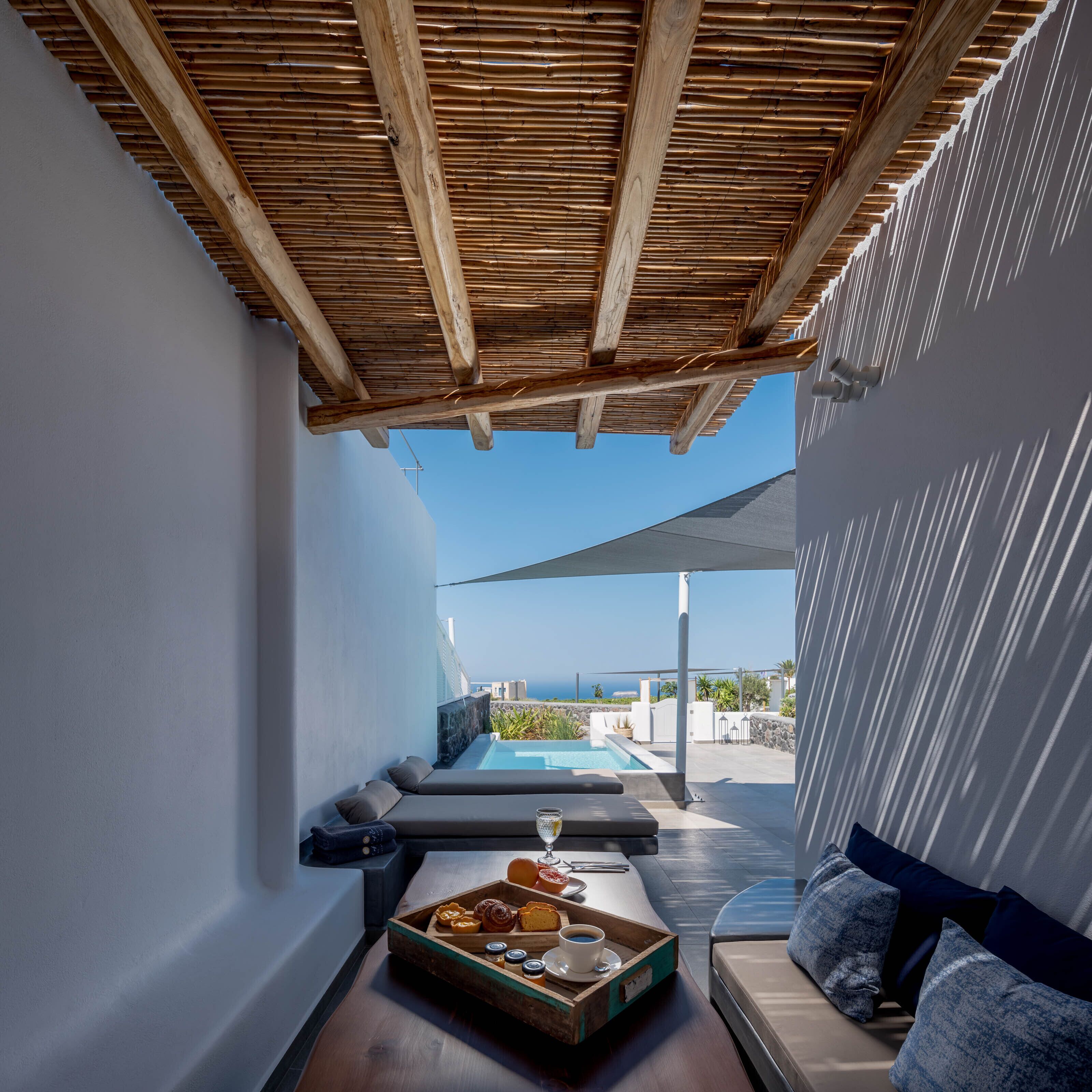 A modern outdoor seating area with a pool, wooden pergola, and a view of the sea.