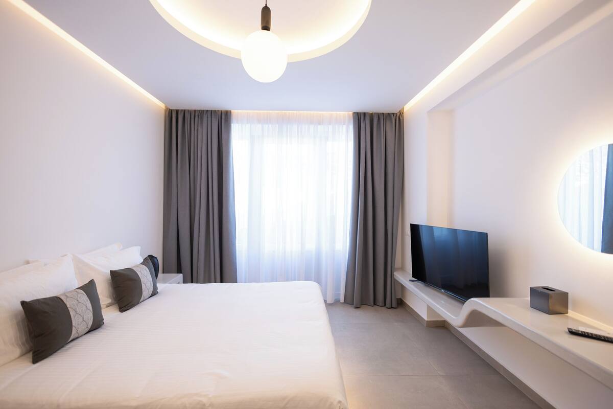 Une chambre d’hôtel moderne dotée d’un grand lit, d’un téléviseur à écran plat et d’une banquette intégrée avec un meuble pour la télévision.
