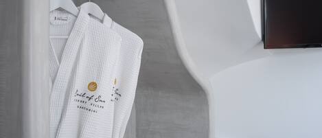 A white robe hanging on a wooden hanger in a bathroom with a white wall and a black object on the wall.