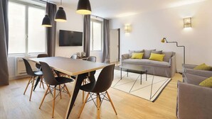 A modern living room with a dining area, a sofa, and a TV mounted on the wall.