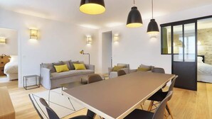 A modern living room with a large dining table, a sofa with cushions, and pendant lighting.