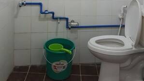 Casa de banho com sanita, chuveiro e balde.
