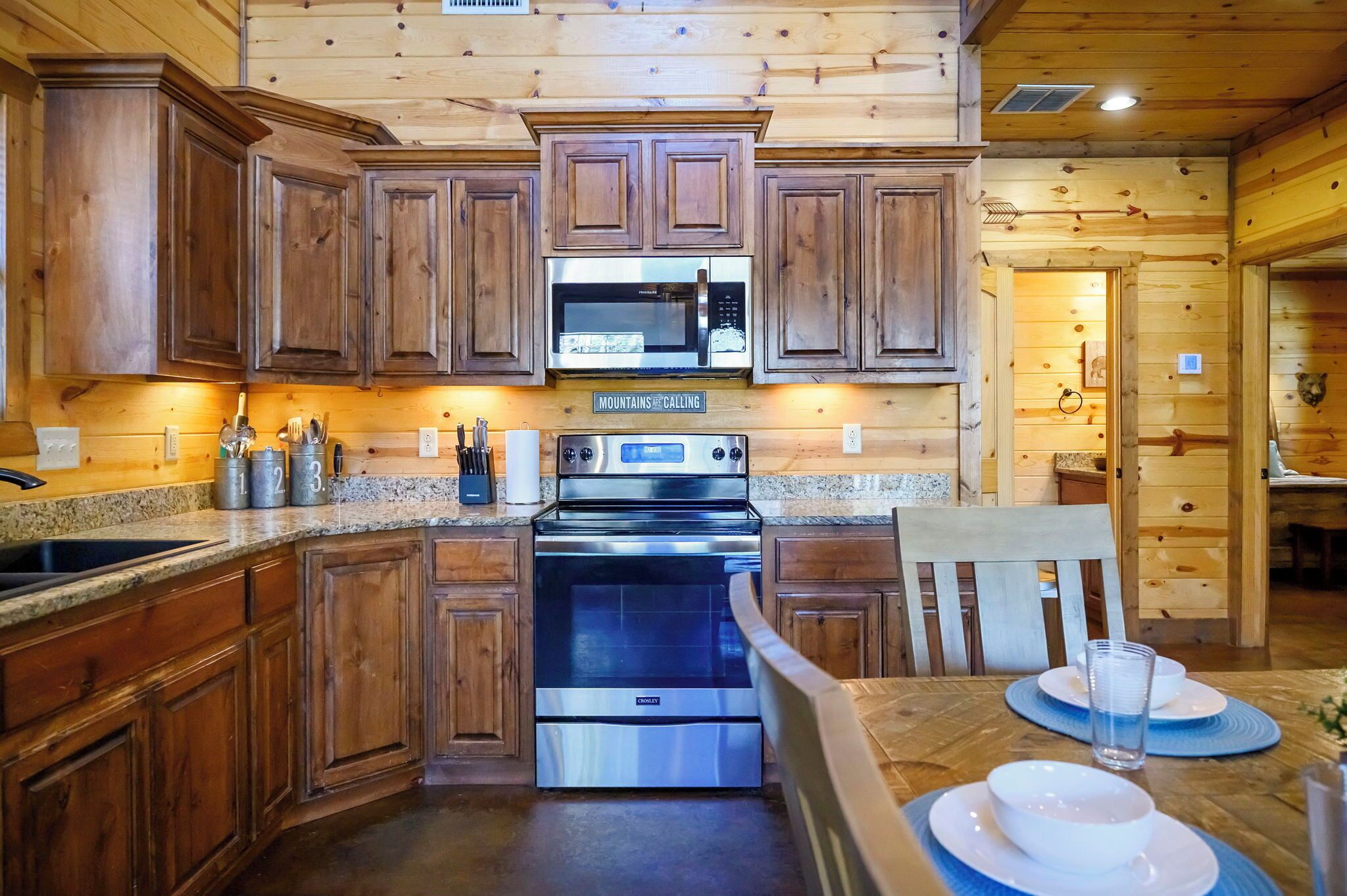 A wooden cabin-style kitchen with a granite countertop, stainless steel appliances, and wooden cabinets.