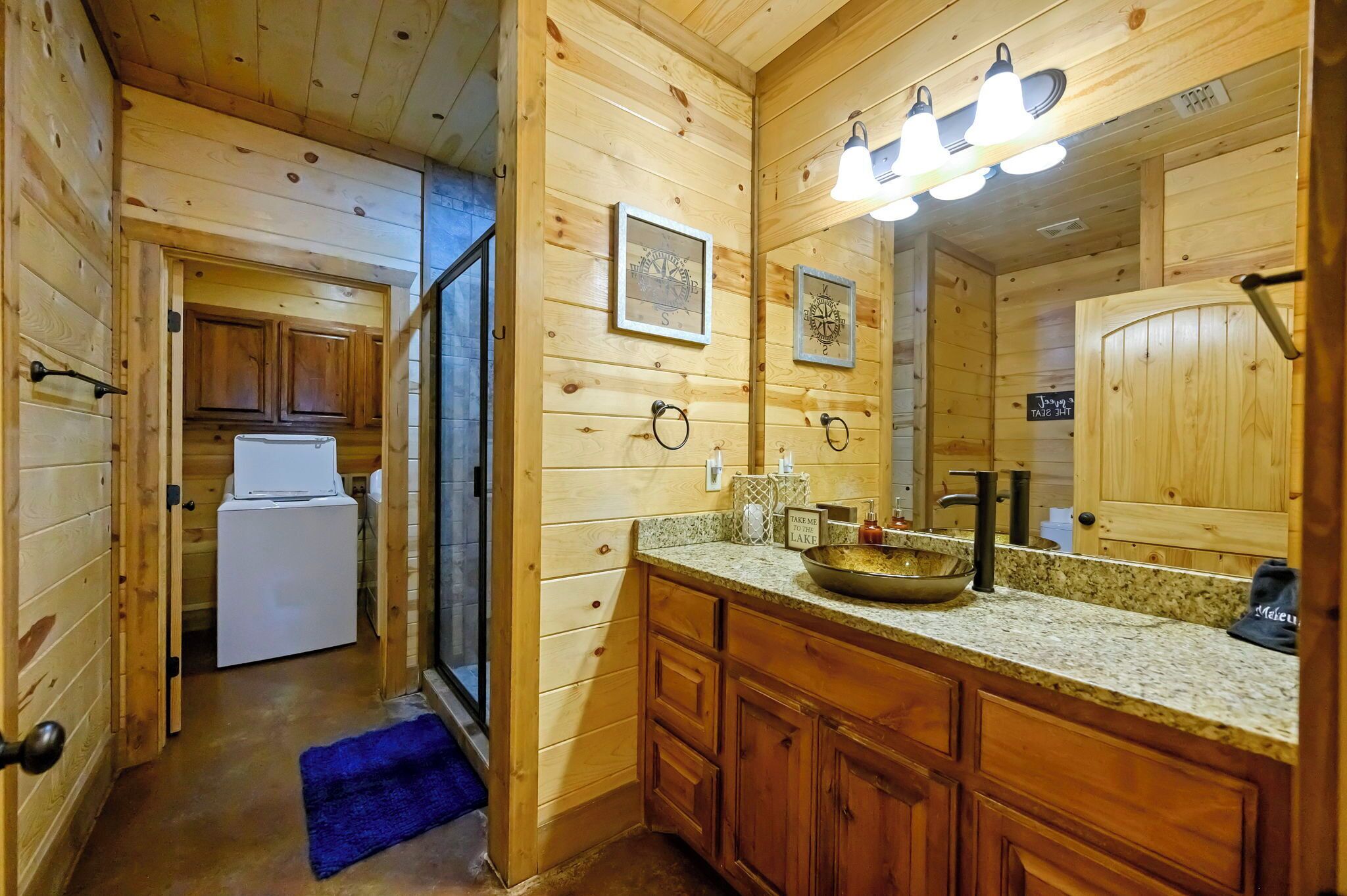 A wooden cabin interior with a kitchen area, a refrigerator, a sink with a bowl, and a mirror with lights.