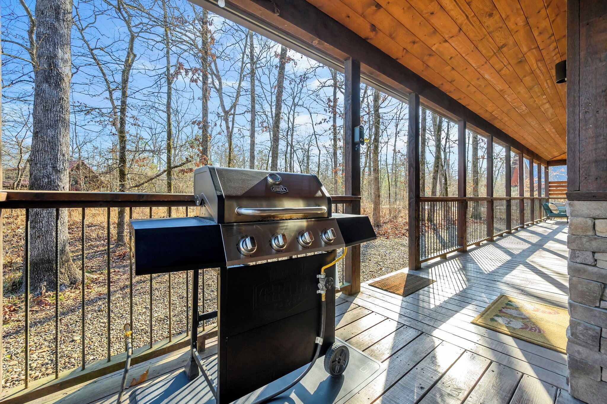 An outdoor grill on a wooden deck with a view of trees and a clear sky.