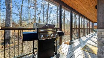 An outdoor grill on a wooden deck with a view of trees and a clear sky.