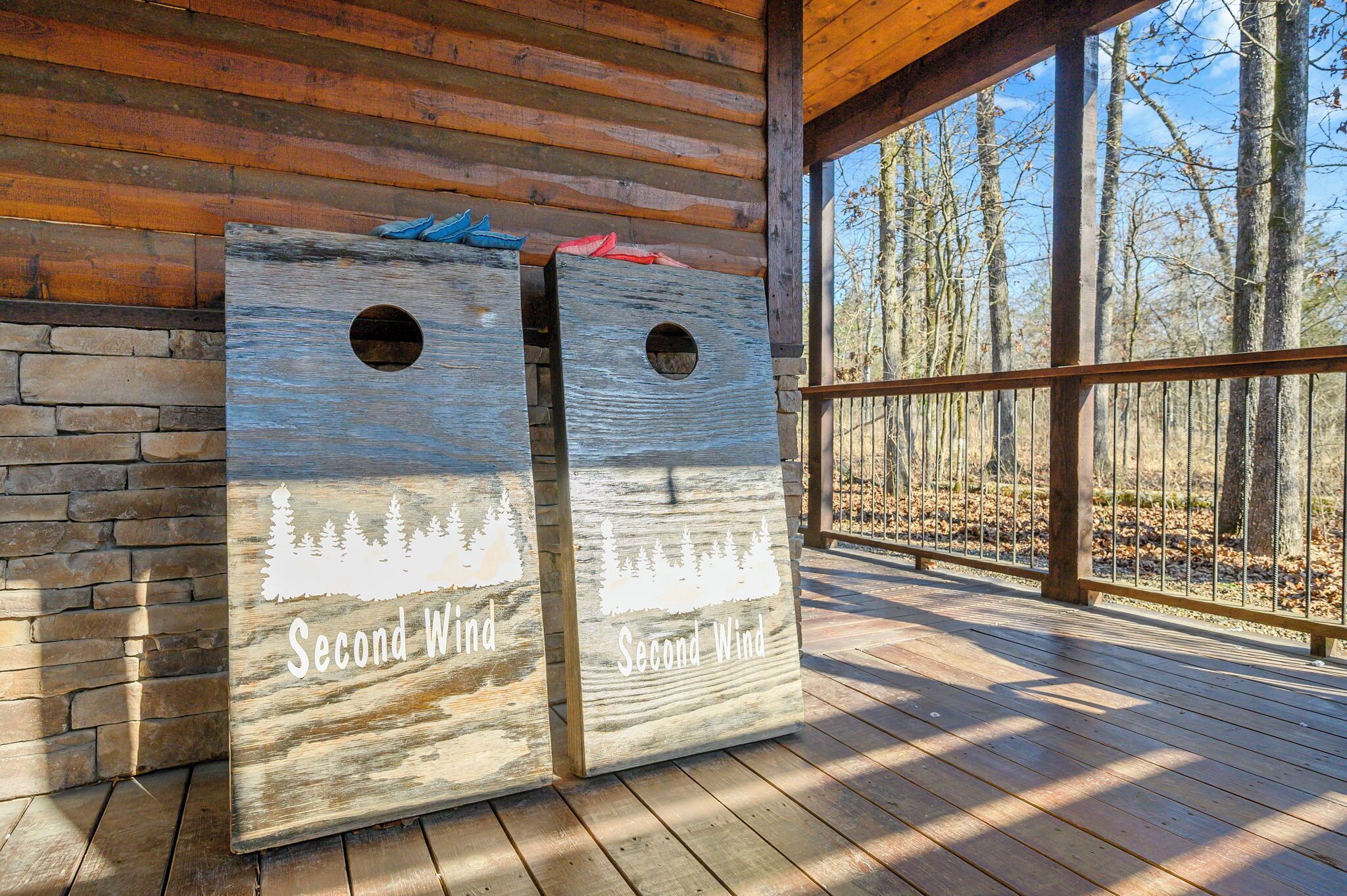 Zwei hölzerne Pflanzkästen mit dem Schriftzug 'Second Wind' und Baumkonturen auf einer Holzdielenveranda mit einer Steinmauer und Blick auf Bäume.