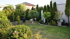 A well-maintained garden with various plants and trees, a lawn, and a white building with a red roof. - Small vacation home with terrace - your oasis of relaxation 🏡🌞 near the Baltic Sea (Ortsamt 2)