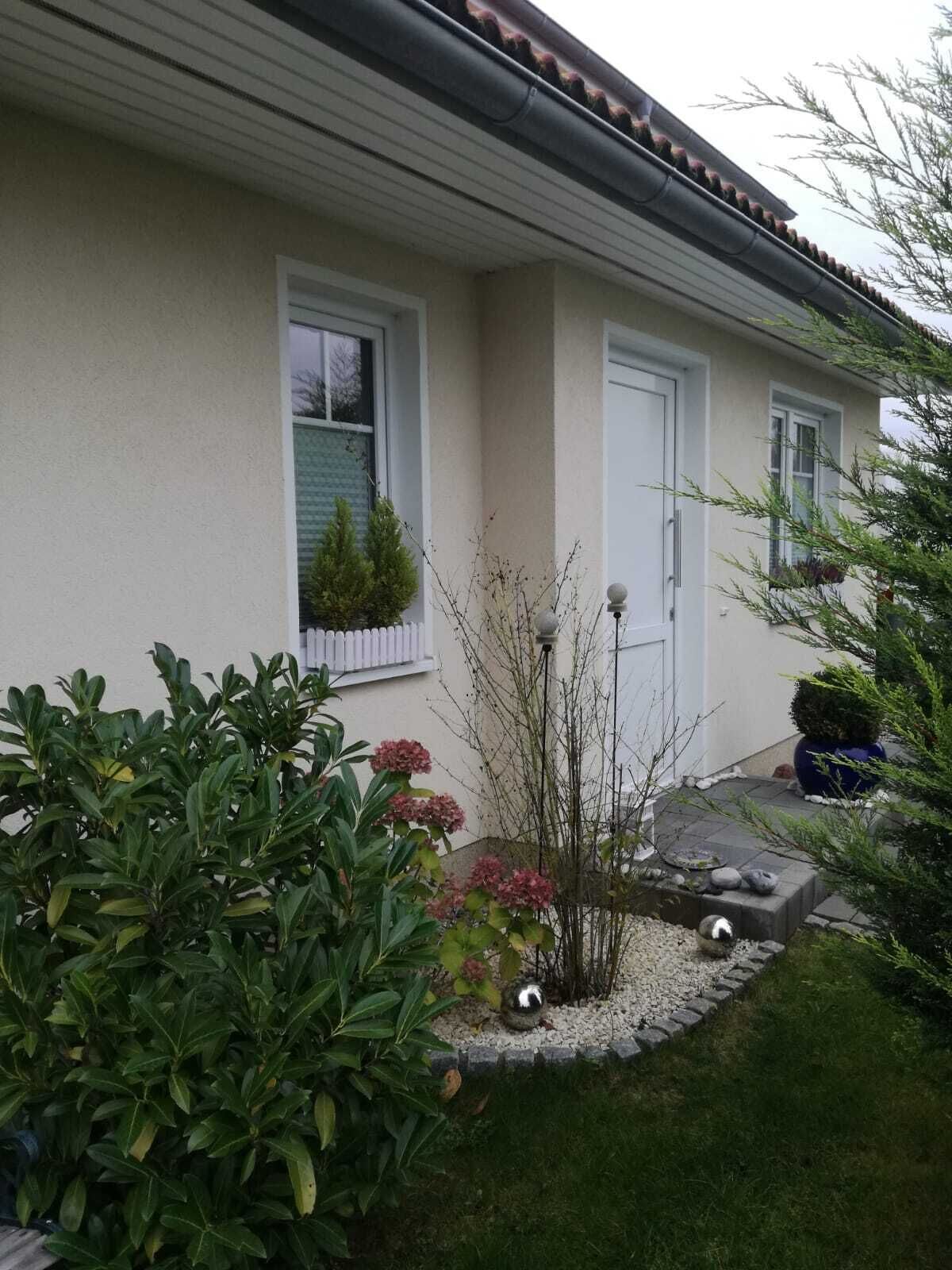 A residential building with a white exterior, a tiled roof, and a small garden area with various plants and a decorative stone feature.