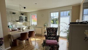 A spacious living area with a dining table, a floral armchair, and a kitchen in the background. - Small vacation home with terrace - your oasis of relaxation 🏡🌞 near the Baltic Sea (Ortsamt 2)