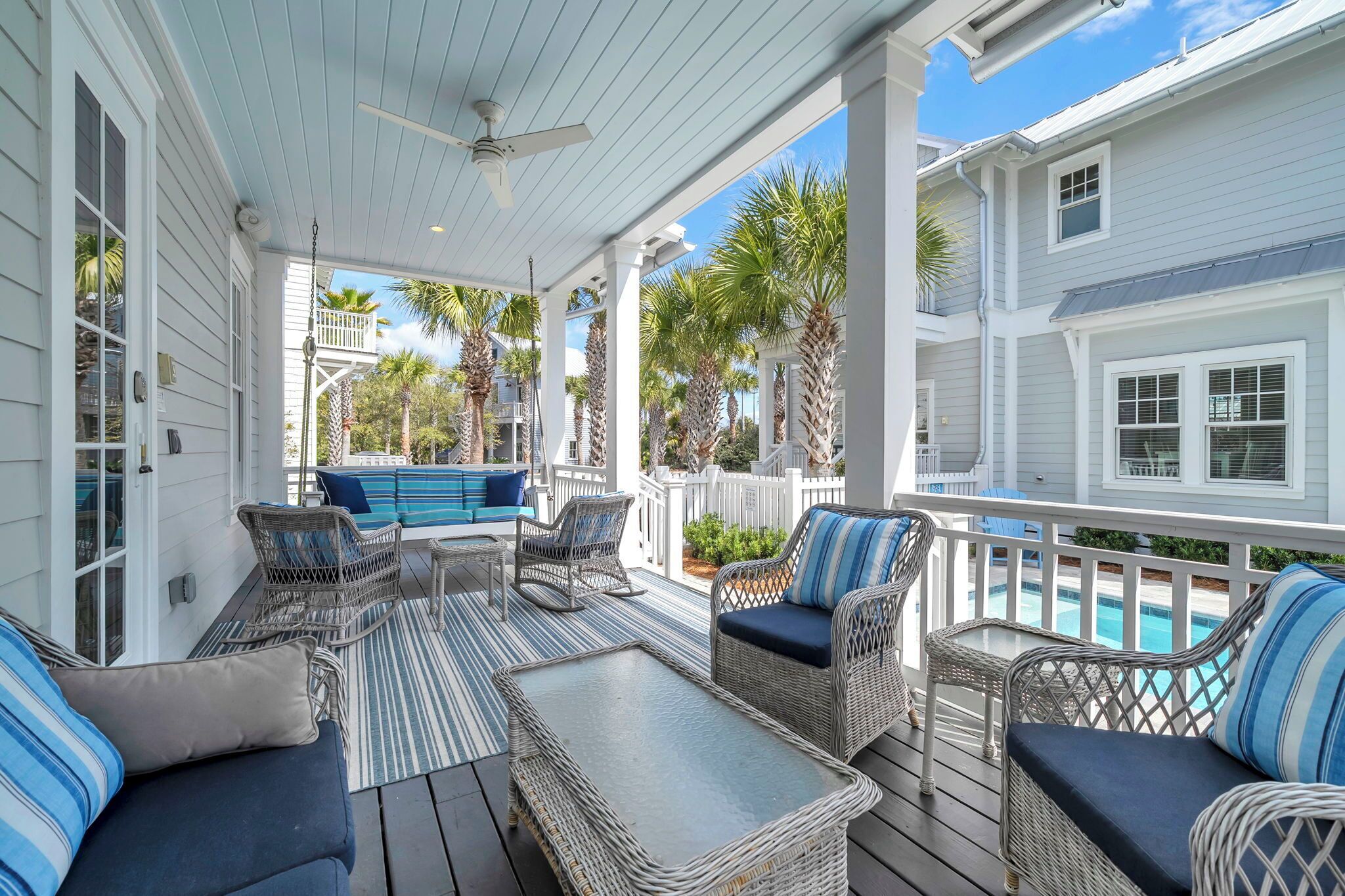 A covered porch with wicker furniture, a ceiling fan, and a view of a pool.