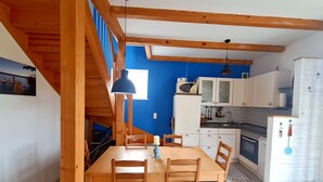 Una cocina con vigas de madera, una mesa de comedor con sillas, una estufa y un refrigerador.