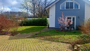 Una casa residencial con un camino de entrada pavimentado, un pequeño jardín con plantas en flor y un cielo despejado.