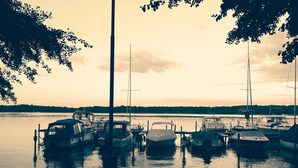 Marina con varias embarcaciones amarradas, rodeada de árboles y una masa de agua tranquila.