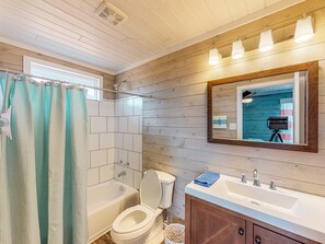 A bathroom with a bathtub, toilet, sink, and a mirror with lights. - Parking for Boat, Close to Restaurants and Shops, Golf Cart Access (Port Aransas)