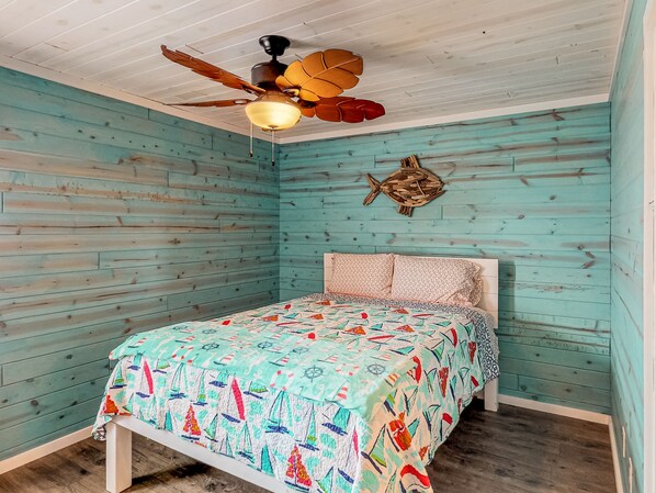 Een slaapkamer met een bed, een plafondventilator en een visdecoratie aan de muur.