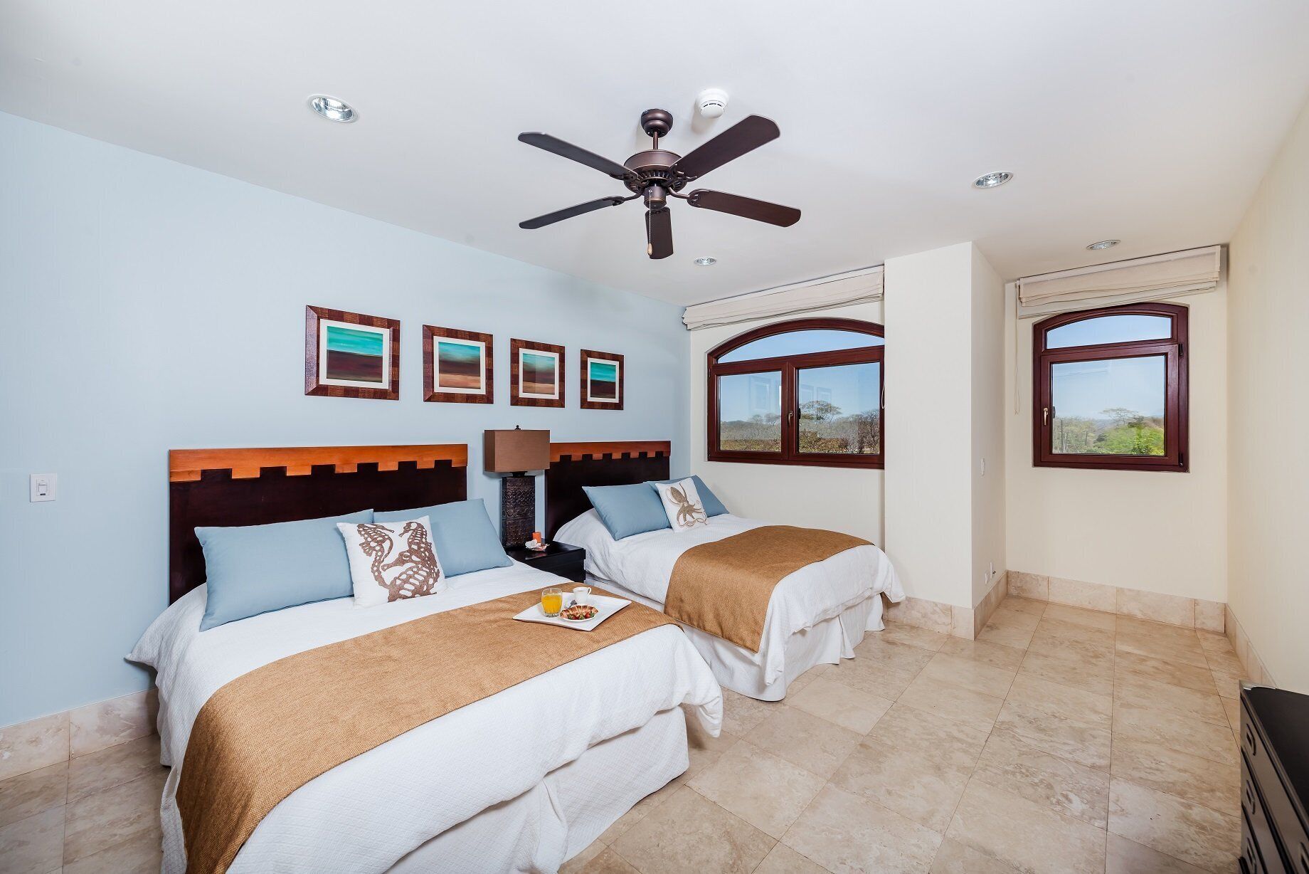 A hotel room with two beds, a ceiling fan, and a large window.