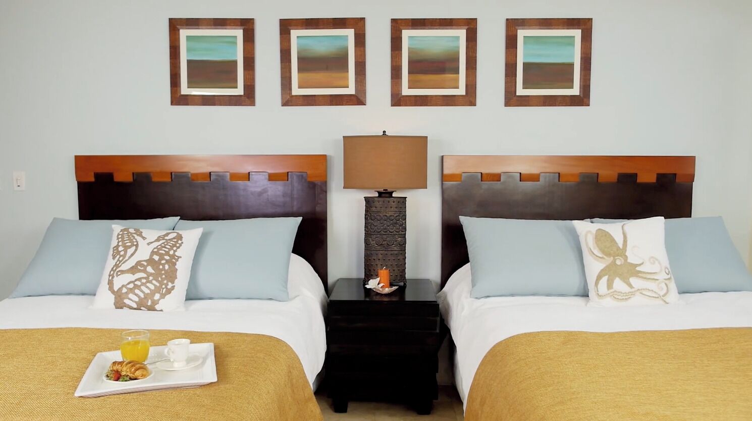 Habitación de hotel con dos camas, una mesita de noche con lámpara y una bandeja con desayuno.