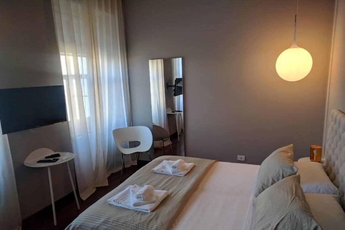 A hotel room with a bed, a chair, a small table, a mirror, and a hanging light fixture.