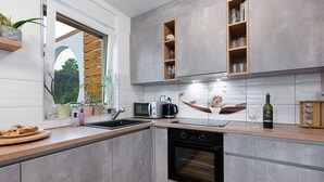 A modern kitchen with grey cabinetry, a built-in oven, a microwave, and a coffee maker. There are plants on the windowsill and a bottle of wine on the counter. - Beautiful home in Bilice (Bilice)