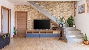 Ein Wohnzimmer mit Flachbildfernseher, Holzunterhaltungseinheit und einer Treppe mit Steinwand.