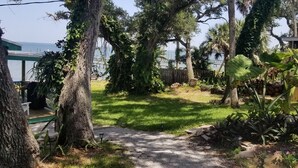 A garden with a gravel path, trees, and a view of the sea. - Gorgeous Riverfront Fishing Cottage in Sebastian, FL - Summer 2026 Specials (Micco)