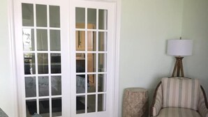 A living room with a grey sofa, a striped armchair, a lamp, and a small ottoman. - Gorgeous Riverfront Fishing Cottage in Sebastian, FL - Summer 2026 Specials (Micco)