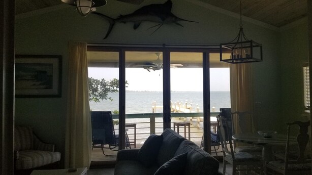 A room with a large sliding glass door leading to a balcony with a view of the sea. - Gorgeous Riverfront Fishing Cottage in Sebastian, FL - Summer 2026 Specials (Micco)
