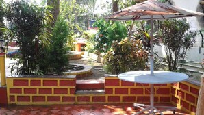 A patio area with a round table and an umbrella, surrounded by brick walls and potted plants. - Maria's House  (Shiroda)