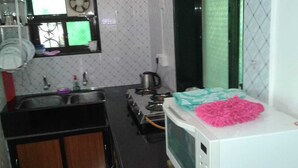A compact kitchen with a sink, stove, microwave, and a small refrigerator. - Maria's House  (Shiroda)