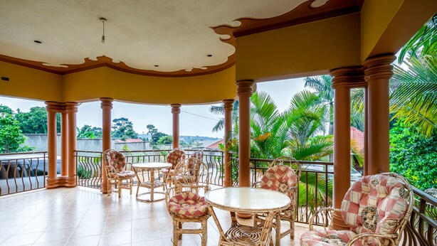 A covered outdoor seating area with wicker furniture and a tiled floor, overlooking a lush garden and residential area. - Airport Side Hotel Entebbe (Entebbe)