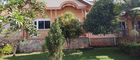 A house with a tiled roof, a small garden with grass and a few trees, and a balcony with a railing.