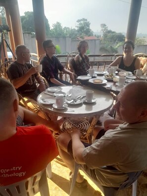 Un groupe de personnes est assis autour d’une table ronde, devant des assiettes, des tasses et des couverts.