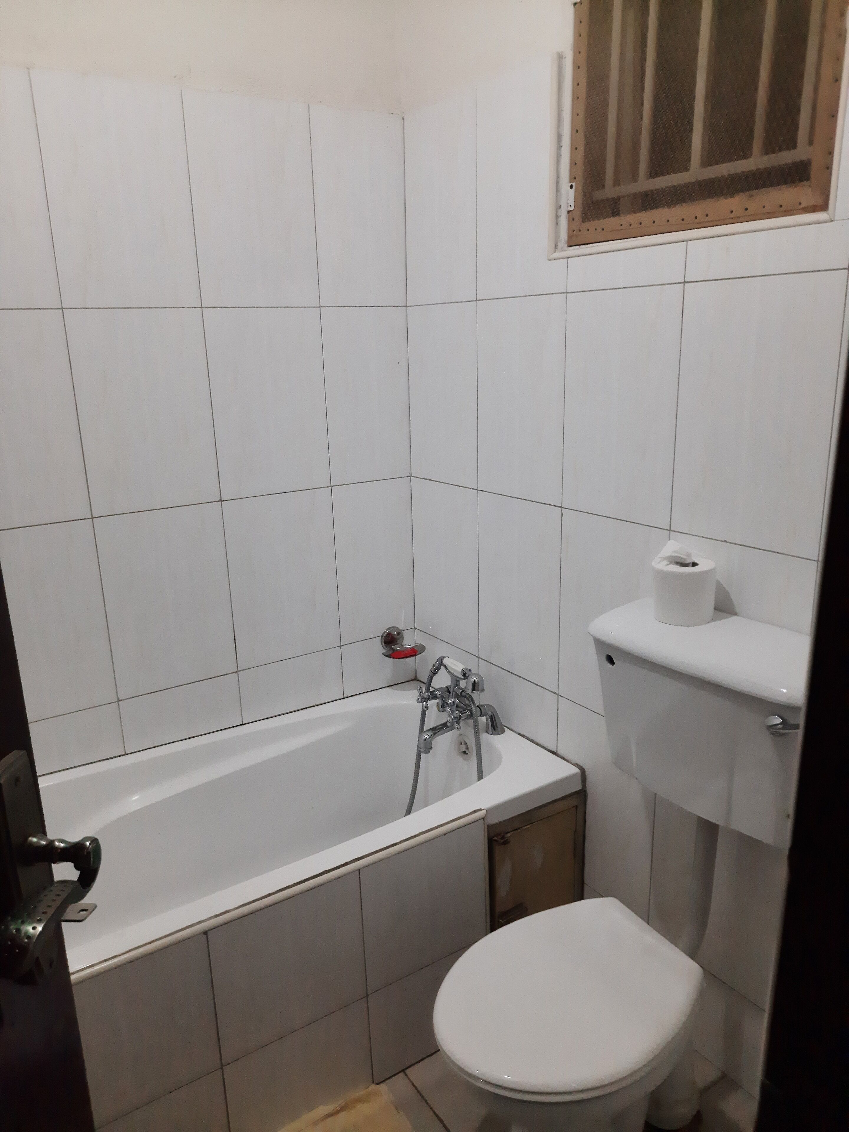 A bathroom with a white bathtub, a toilet, and a window with a wooden frame.