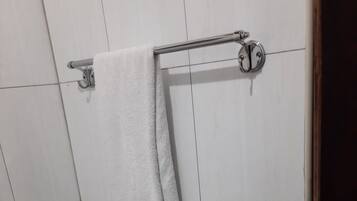 A bathroom with white tiled walls, a towel rack, a handrail, and a toilet paper holder.