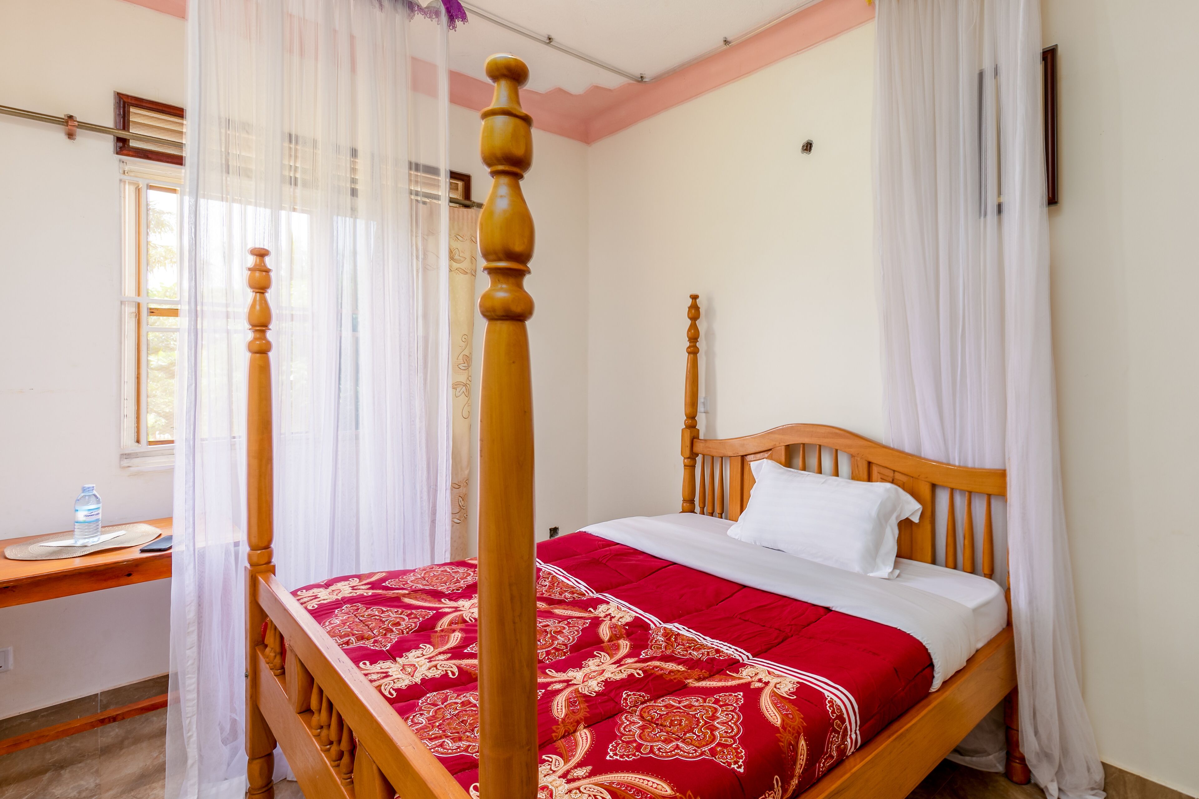 Una cama con dosel con edredón rojo y blanco, cabecera de madera y cortinas blancas.