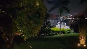 A nighttime view of a well-lit garden area with a parked car and a building in the background. - Airport Side Hotel Entebbe (Entebbe)