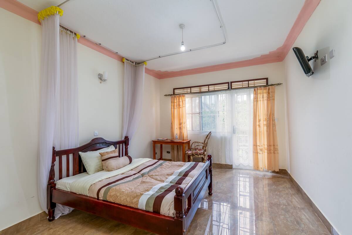 A bedroom with a wooden bed, a nightstand, a chair, and a window with curtains.