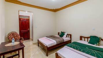 A bedroom with two beds, a wooden table with a water bottle, and a red door.