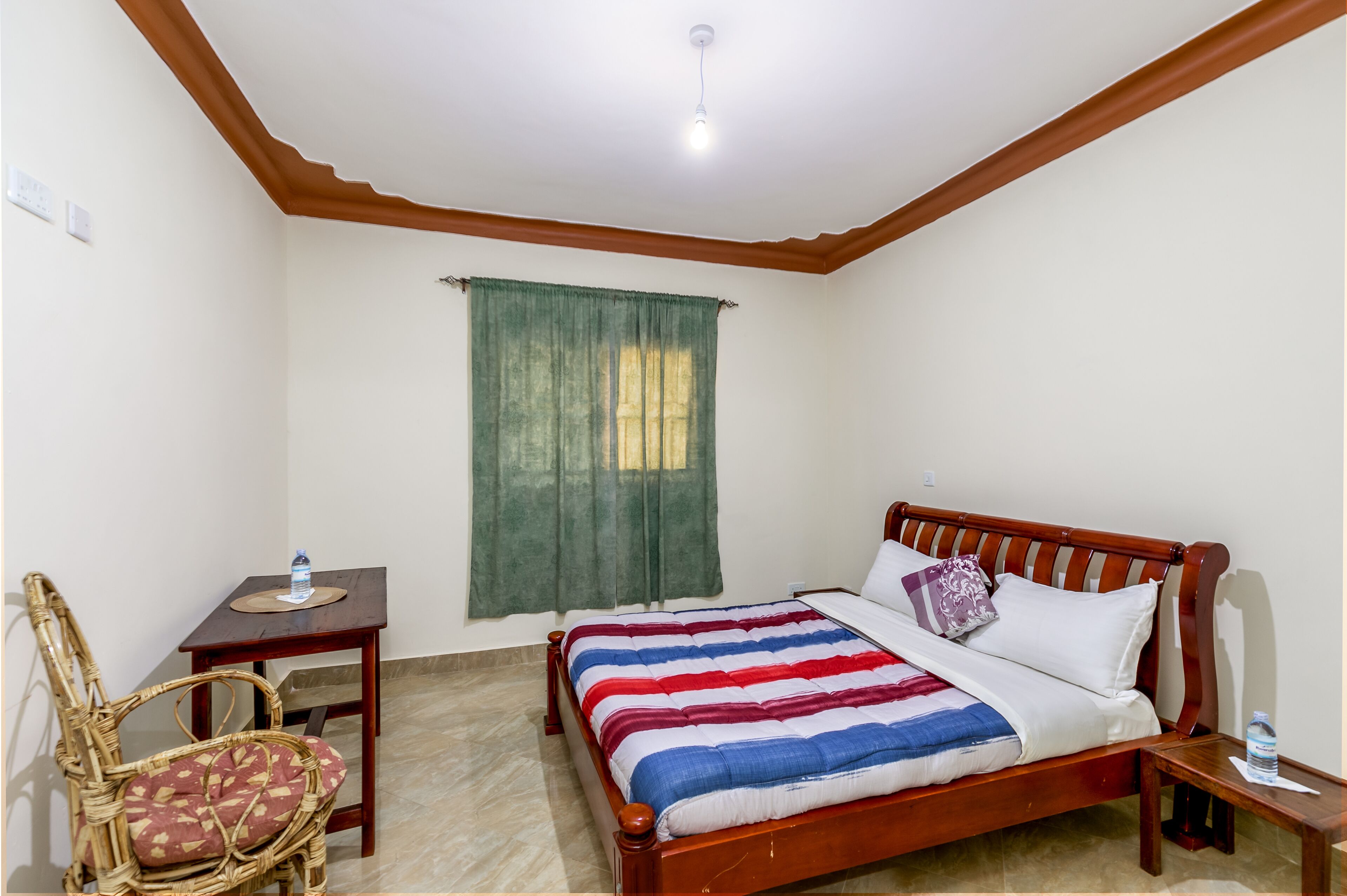 A bedroom with a wooden bed, a small table, a chair, and a window with curtains.
