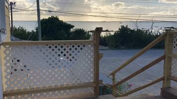 A wooden deck with a white lattice railing, a wooden staircase, and a view of the sea.