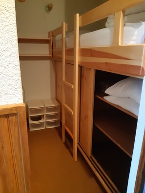 Cama litera con estructura de madera y un estante en la parte inferior. Hay cajones blancos para guardar cosas debajo de la cama.