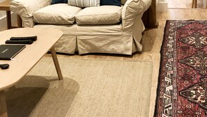 A living room with a beige sofa, a wooden coffee table, a patterned rug, and a staircase. - Cotswold Cottage, with wood burning stove and private courtyard garden (Northleach)