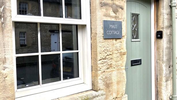 A stone building with a large window and a door labeled "MALT COTTAGE". - Cotswold Cottage, with wood burning stove and private courtyard garden (Northleach)