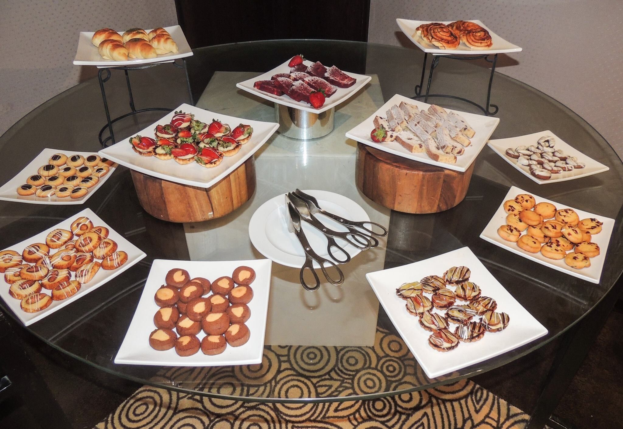A round glass table with various food items and a pair of scissors in the center.
