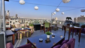Une terrasse sur le toit, aménagée avec des espaces de détente en plein air, des plantes en pot et des luminaires sphériques suspendus.