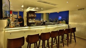 Un espace bar avec un barman, un comptoir où sont exposées différentes bouteilles et une vue sur la ville par la fenêtre.