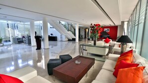 Un hall d’entrée spacieux comprenant un comptoir d’accueil, un escalier et un espace détente avec une table basse et des canapés.